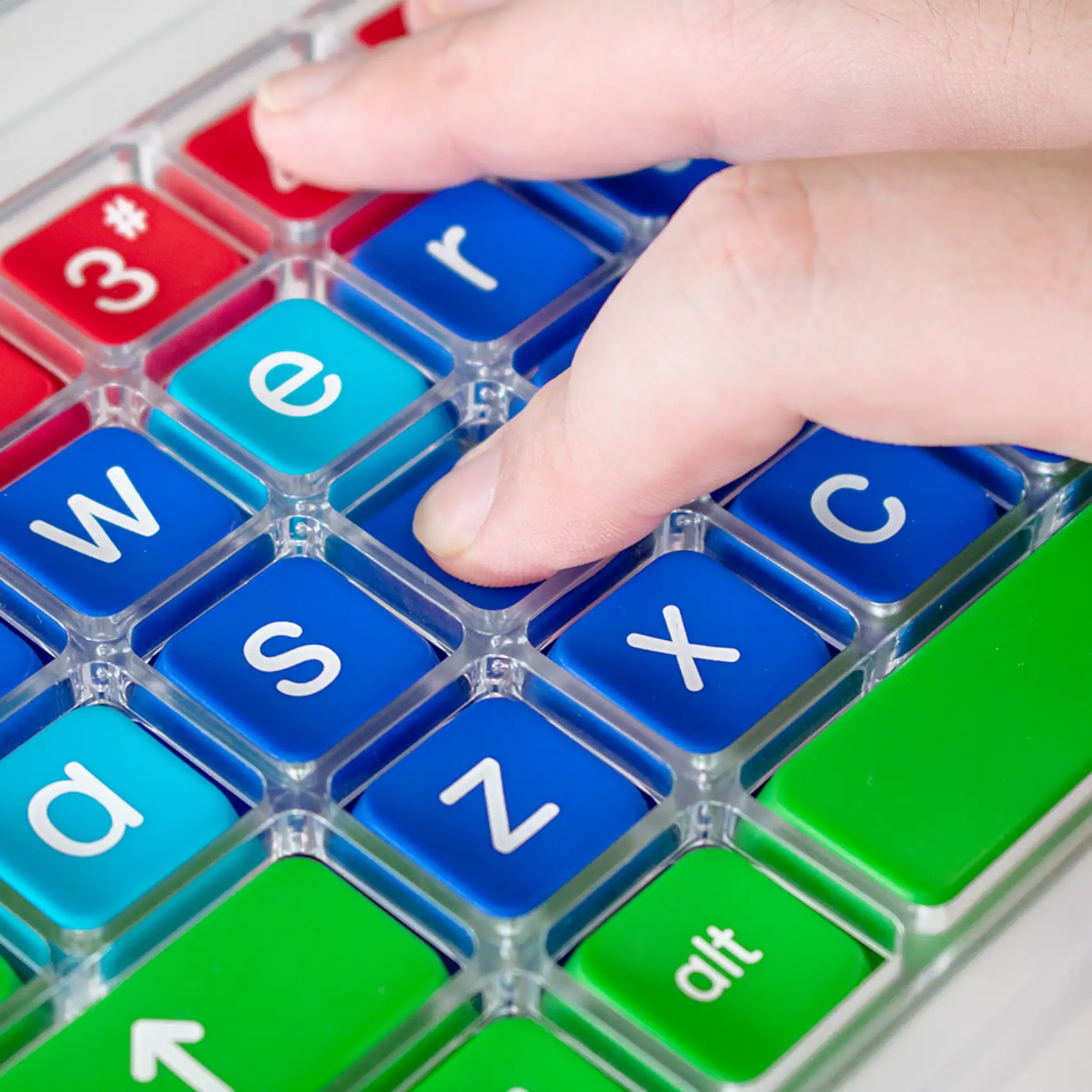 Close up image of a hand with a finger pressing a key on a colourful keyboard. The keyboard has a clear perspex keyguard separating the keys.