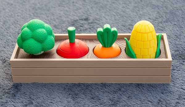 A small 3D printed raised garden bed with a broccoli, radish, carrot and corn sitting in the garden bed.