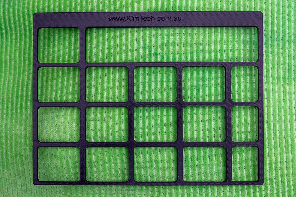 A black 3D printed keyguard for Grid for iPad VocoChat page set displayed on a green cushion.