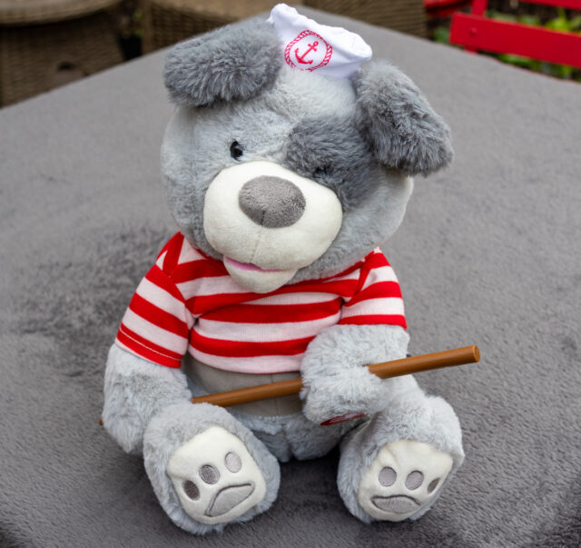 A bear dressed in a red and white striped t-shirt holding an oar in its paw.