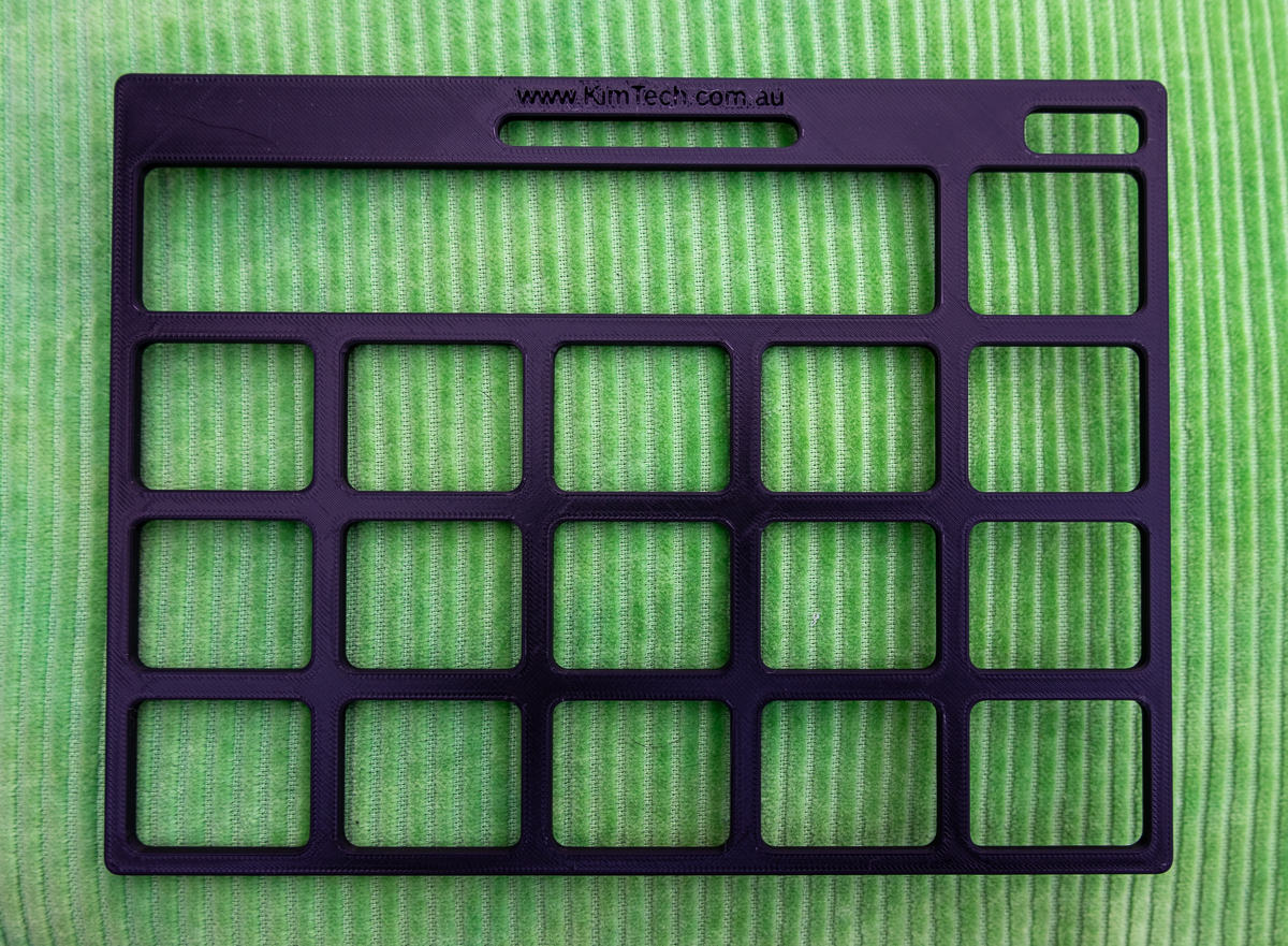 A black 3D printed keyguard for SimPODD page set displayed on a green cushion.