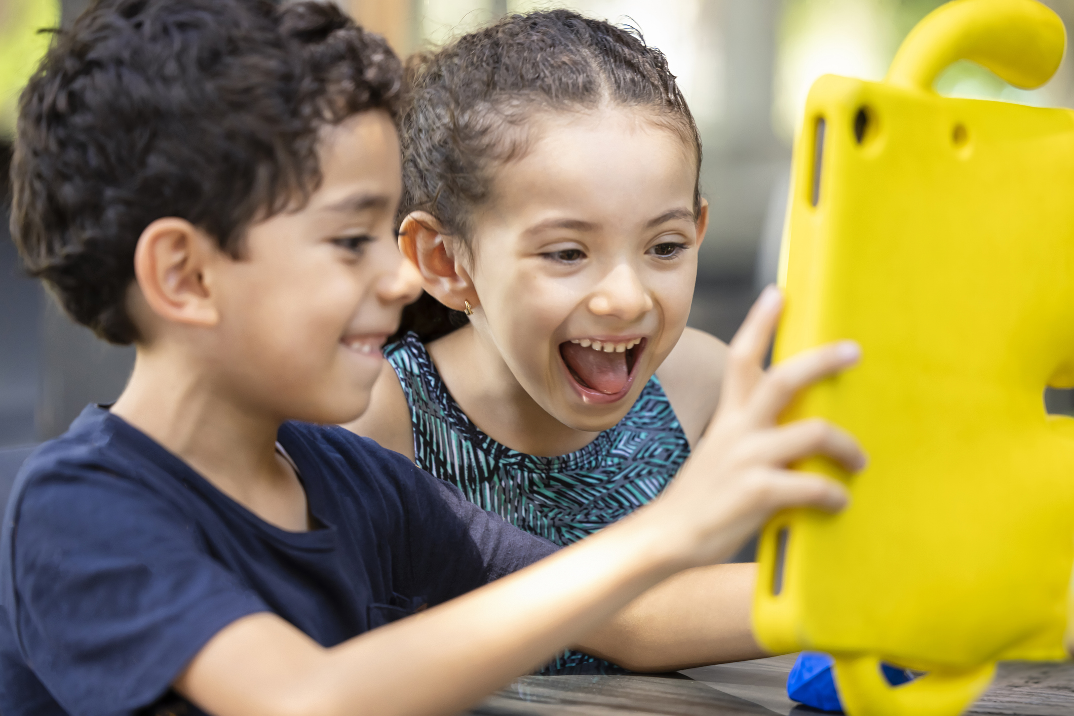 A young white boy and white girl looking at an iPad together and laughing.