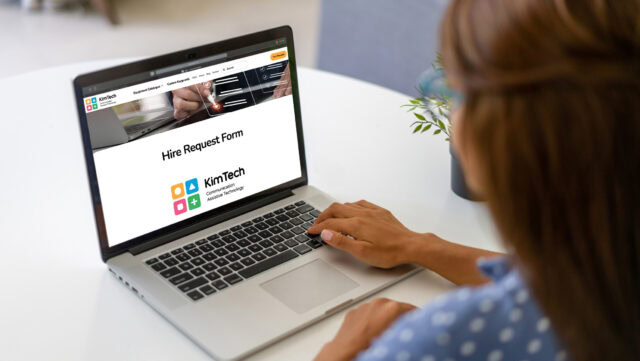 A white woman with her back to the camera sitting at a desk with a laptop open displaying the KimTech equipment hire request form.