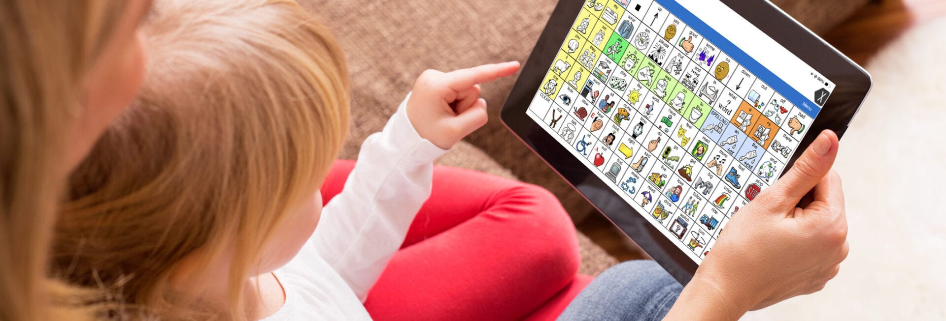 Child using an iPad with an AAC communication app (symbol-based grid) while interacting with an adult, supporting speech and communication development.