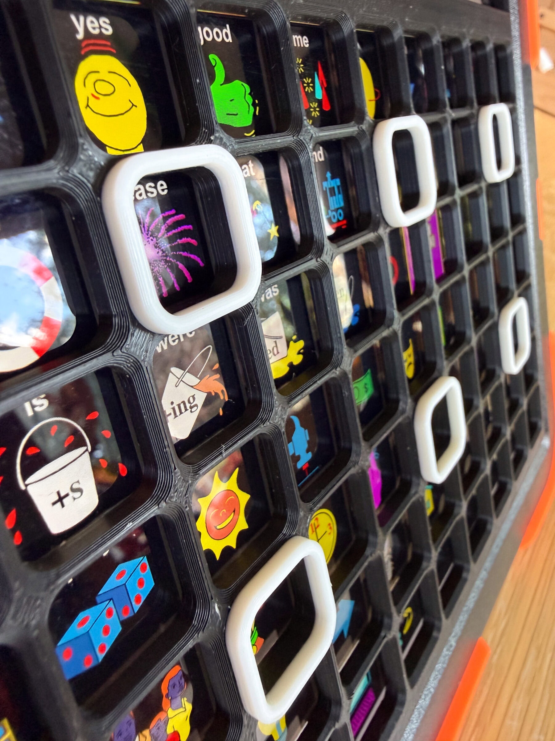 Close-up of a custom 3D-printed tactile AAC keyguard fitted over an iPad communication app LAMP Words for Life, showing raised borders around individual symbol buttons to support accurate access.