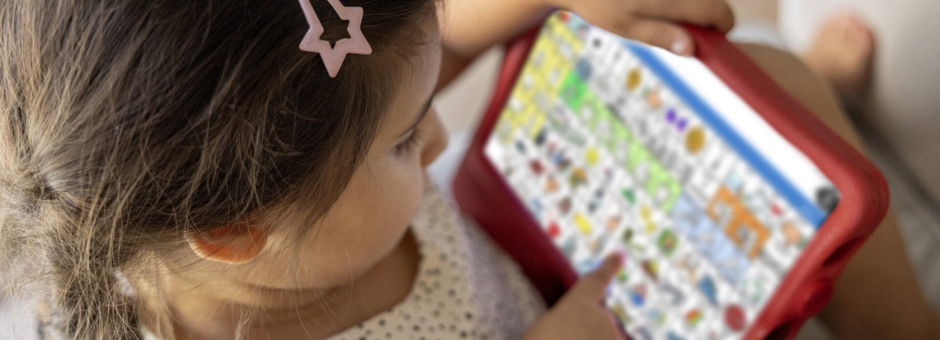 A young girl with an iPad displaying the AAC app LAMP Words for Life. She is pointing to a symbol within LAMP.