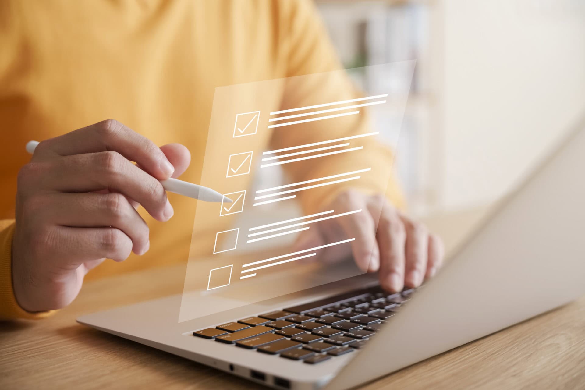 Person using a stylus while working on a laptop, with a transparent digital checklist displayed above the keyboard showing several completed tasks and one unchecked item, representing online forms, assessments, or task management.
