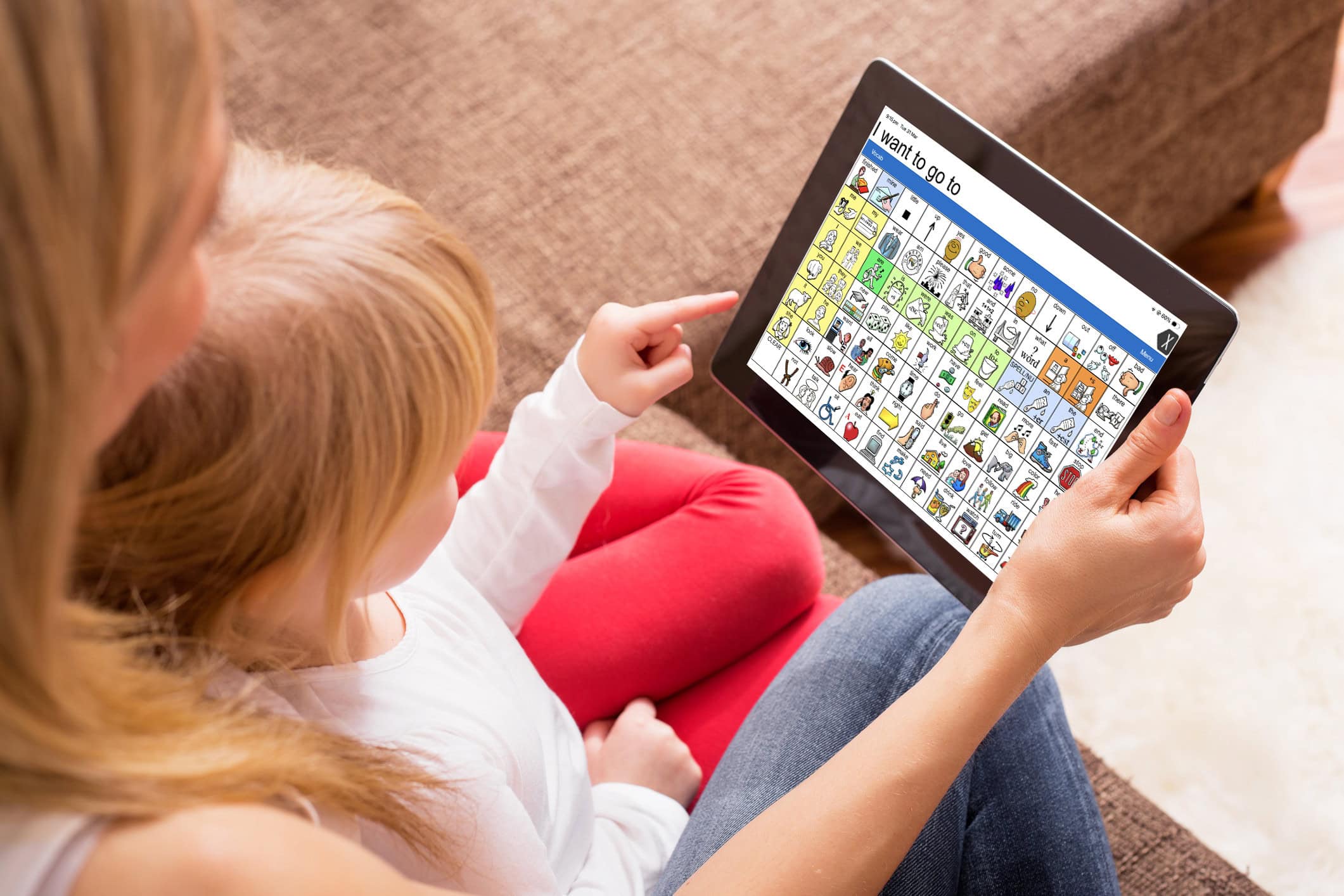 Child using an iPad with an AAC communication app (symbol-based grid) while interacting with an adult, supporting speech and communication development.